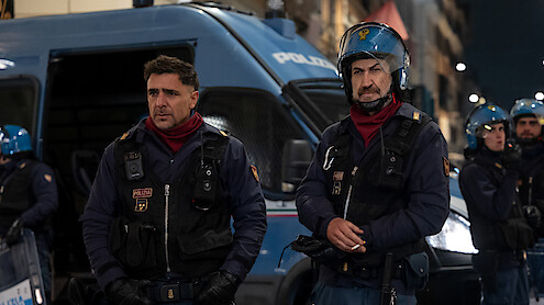 Adriano Giannini as Michele Nobili and Marco Giallini as Mazinga dress in police uniforms and stand outside in front of a police van in the series 'Public Disorder.'