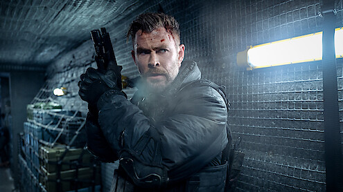 Chris Hemsworth as Tyler Rake with a bruised face and tactical gear holding a handgun, standing alert in a dimly lit, metal-walled corridor with supplies and fluorescent lighting, appearing ready for action or conflict.