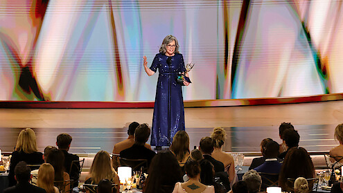 Uma mulher usando um vestido azul aparece no centro do palco recebendo uma premiação no Emmy 2026