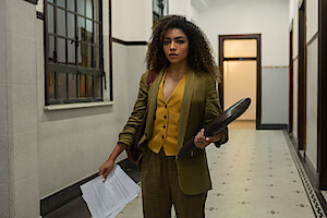 Atriz Any Gabrielly segura folhas de papel e uma pasta em um corredor da faculdade de advocacia