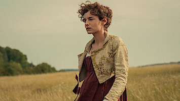 Woman in historical dress standing in a field with tall grass, trees in the background, and a cloudy sky, creating a calm, pastoral setting.