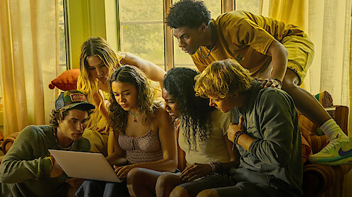 The cast of Outer Banks gathered around a laptop