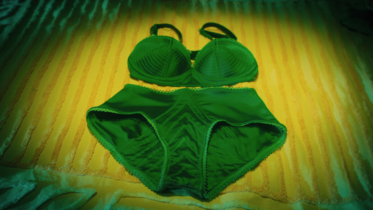 Green women's bra and underwear set laid out on a yellow-striped bedspread under soft lighting.