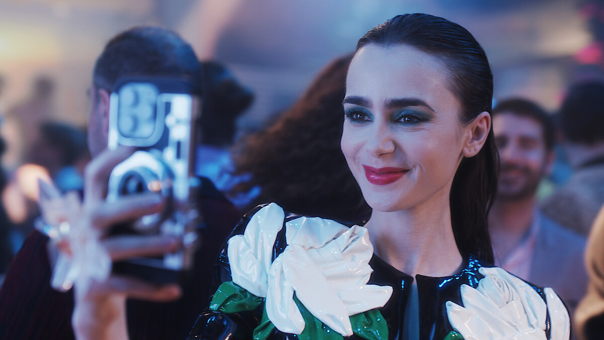 Lily Collins as Emily takes a photo with her cell phone in season 4 of “Emily in Paris”