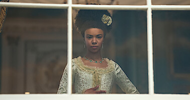 queen charlotte stands in front of a window thinking 