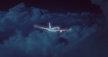 A silhouette of a plane against a dark, cloud-filled sky.