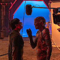 Actor in monster makeup faces another actor on a film set, creating an intense, behind-the-scenes atmosphere.
