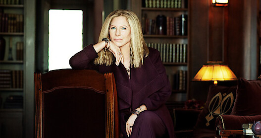 Photo of Barbara Streisand sitting in a room with books in background.