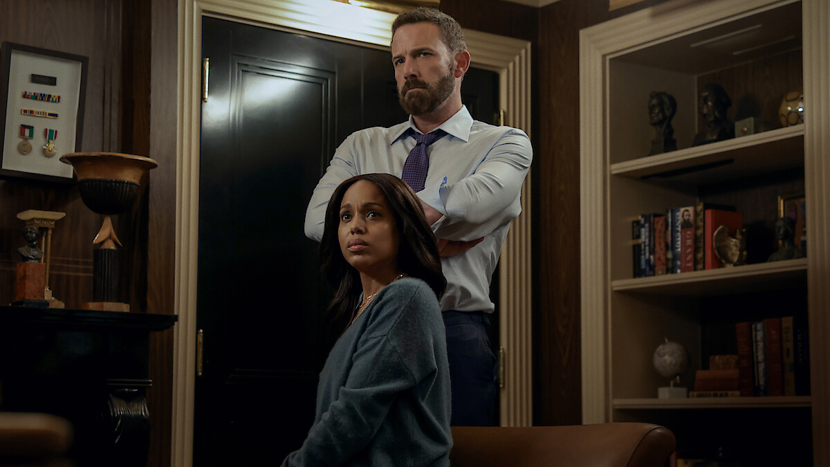 A serious man stands with arms crossed behind a seated woman in an elegant office lined with bookshelves, awards, and dark wood decor. Both appear deep in thought, suggesting a tense or important conversation.