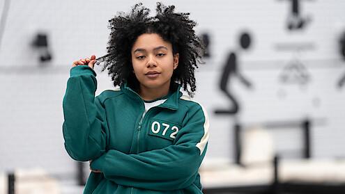 The winner of Squid Game the Challenge Season two standing in front of a pink graphic, welcoming people into her home