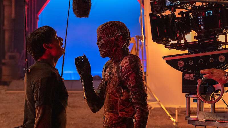 Ator com maquiagem de monstro encara outro ator em um set de filmagem, criando uma atmosfera intensa de bastidores.