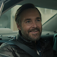 Will Forte as Gilbert Power smiles in the backseat of a car in 'Bodkin'