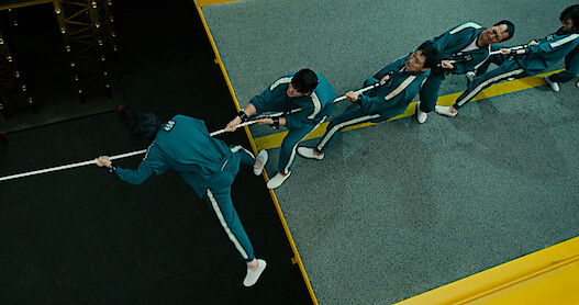 The characters of Squid Game playing a very stressful and critical game of tug-o-war