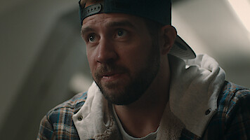  A closeup of a man in wearing a backward black baseball cap and a hooded flannel sweatshirt in 'The Twister: Caught in the Storm'