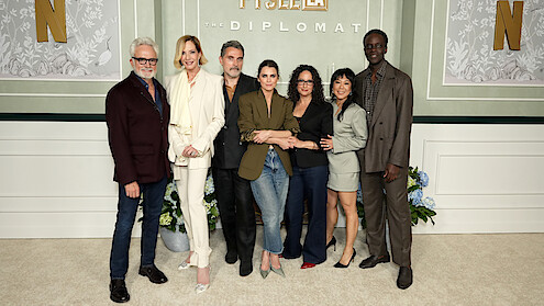 Bradley Whitford, Allison Janney, Rufus Sewell, Keri Russell, Debora Cahn, Ali Ahn and Ato Essandoh stand together posing for a group photo at an event for "The Diplomat," in front of a green and white decorative backdrop with Netflix branding.