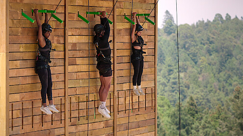 Quori-Tyler Bullock, Chase DeMoor, and Georgia Hassarati hanging from a climbing wall during a challenge