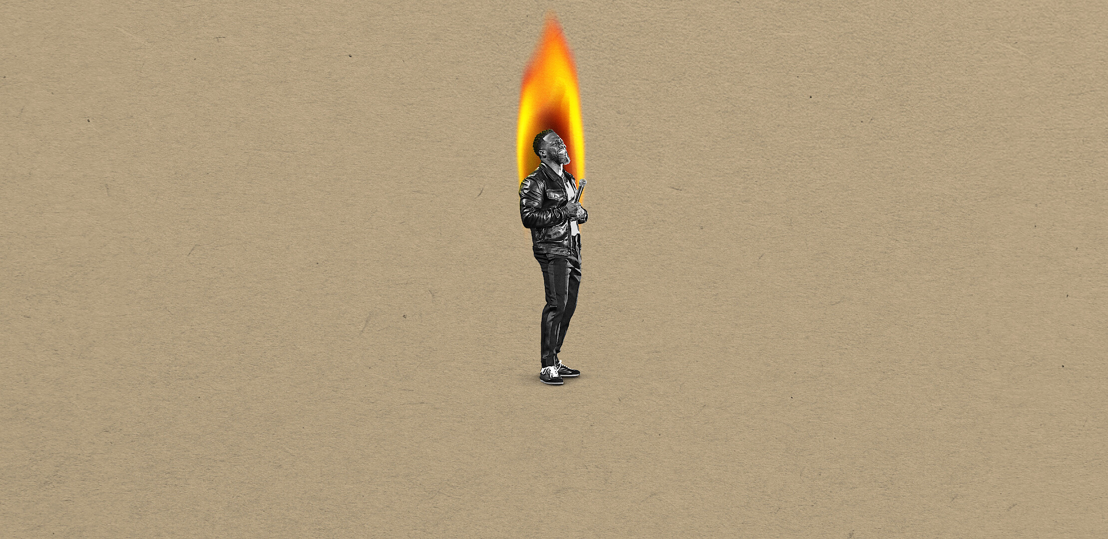 Kevin Hart in black-and-white stands on a tan background, with their head replaced by a large bright flame, suggesting a surreal or artistic concept.
