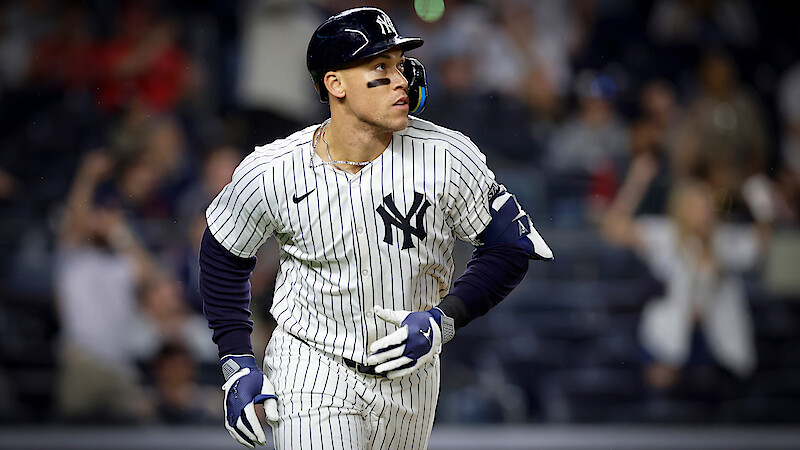 New York Yankees baseball player in pinstripe uniform runs on field during a night game; blurred crowd in the background creates an energetic, competitive atmosphere.