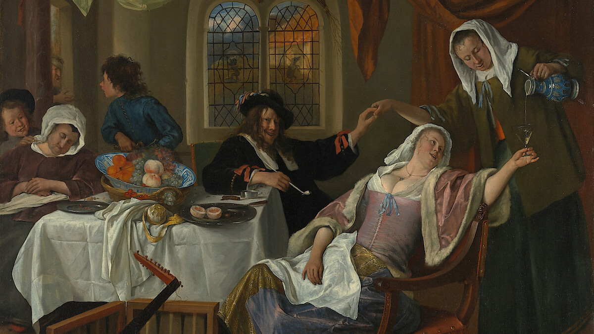 Group of people in 17th-century clothing at a dining table in a richly decorated room; a woman reclines in a chair as another pours her a drink, with food and musical instruments nearby.