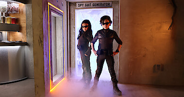 Everly Carganilla as Patty Tango-Torrez and Connor Esterson as Tony Tang-Torrez stand in front of the spy suit generator in 'Spy Kids: Armageddon.'
