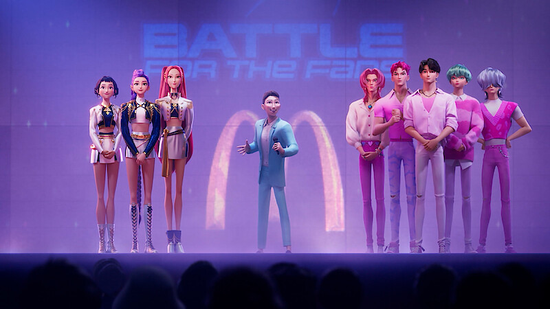 Animated characters stand on a brightly lit stage, divided into two groups, with a host in the center. They face an audience, under a "Battle of the Fans" sign, creating a competition atmosphere.