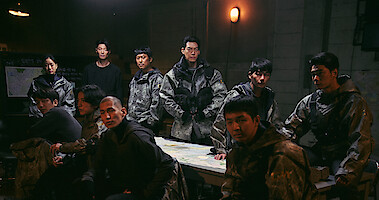 Several people wearing futuristic tactical gear gather around a table.
