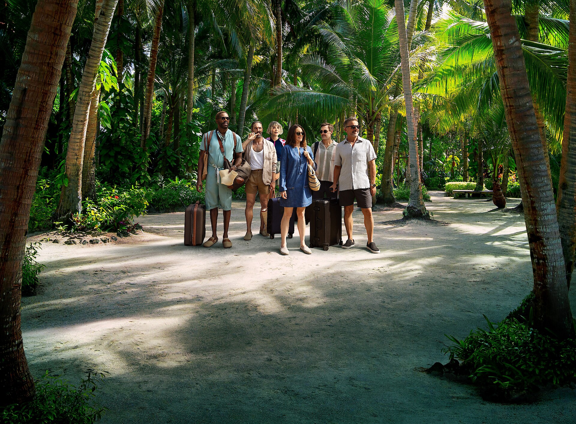 The Four Seasons - the cast of The Four Seasons standing in a jungle carrying suitcases. 
