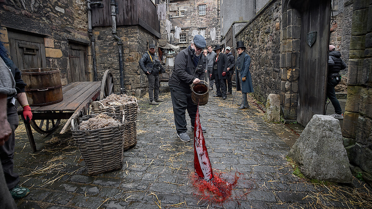 Guillermo del Toro throws a bucket of blood into cobblestoned streets on the set of Frankenstein.