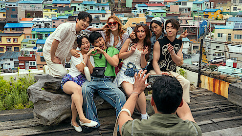 A group of friends poses happily for a photo on a rooftop with colorful houses in the background, showing a lively urban setting and cheerful atmosphere.