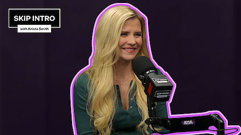 Elizabeth Smart sits smiling in front of a microphone during a podcast recording for "Skip Intro with Krista Smith." The background is purple, and the podcast logo appears in the top left corner.