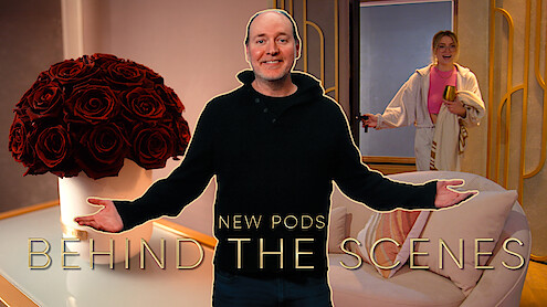 Production Designer Dave Edwards stands with his arms outstretched in front of a pod room. A vase of roses sits on the left, while Madison enters through the door on the right.