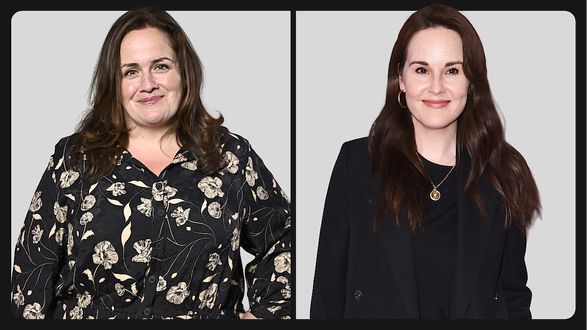 Two women posed side by side against a plain light gray background, one wearing a floral blouse and the other in a black blazer, both smiling at the camera in a studio setting.
