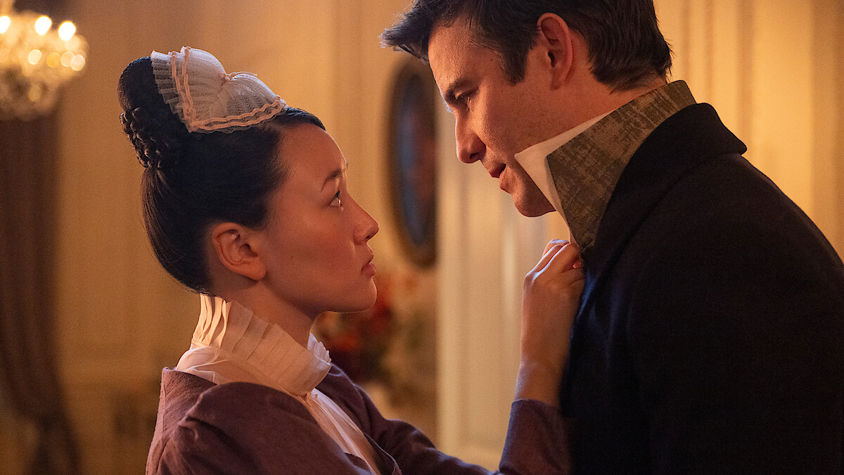 A woman in period costume faces a man in a formal suit in a softly lit, elegant Victorian-era room, with intense expressions suggesting a serious or intimate conversation.