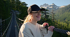 Alexandra Breckenridge as Mel Monroe smiles on a rope bridge with a mountain in the background in Season 5 of ‘Virgin River.’