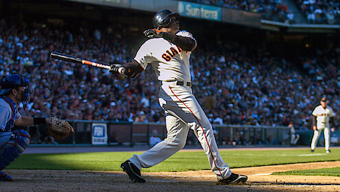 Barry Bonds in a Giants uniform swinging bat during a sunny game, catcher and umpire nearby, large crowd in stadium background.