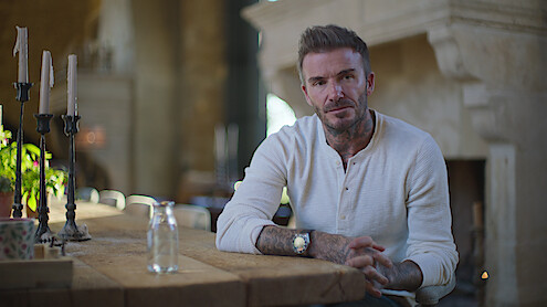 David Beckham in a white shirt sitting at a kitchen table. 
