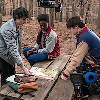 Four teenagers gather at a wooden picnic table in a forest during autumn, studying a map.