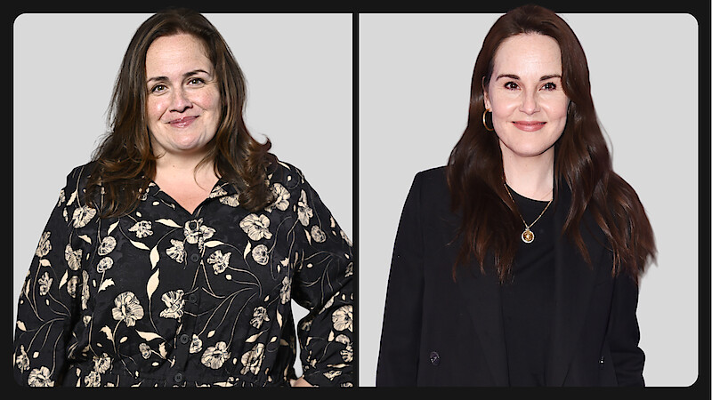 Two women posed side by side against a plain light gray background, one wearing a floral blouse and the other in a black blazer, both smiling at the camera in a studio setting.