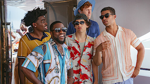Five men in colorful summer shirts and sunglasses talking and laughing on a yacht, bright daylight, casual vacation atmosphere.