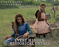 Two girls in prairie dresses sit outdoors beside rustic wooden tables and vintage cooking tools in a grassy field, reenacting a historical pioneer camp scene. A campfire is visible in the foreground, trees in the background.