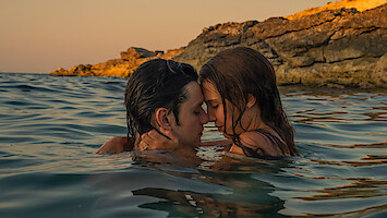 A couple embracing closely in the water near rocky cliffs at sunset, creating a romantic and intimate atmosphere with warm natural lighting.
