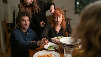 Azazel Jacobs sits in a brown-toned living room with Natasha Lyonne, who stretches back on a couch in a sweatsuit and points at Jacobs.