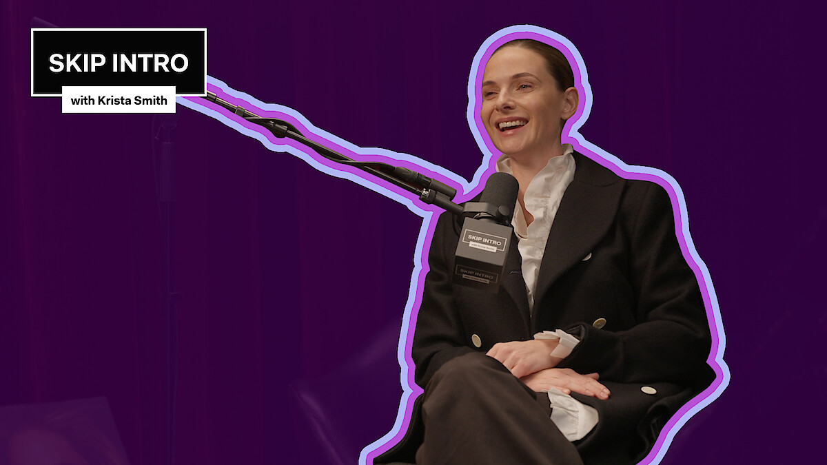 Rebecca Ferguson smiling and sitting in a podcast studio, speaking into a microphone with "SKIP INTRO with Krista Smith" logo in the corner, outlined in purple, set against a dark purple background, creating a lively and engaging atmosphere.
