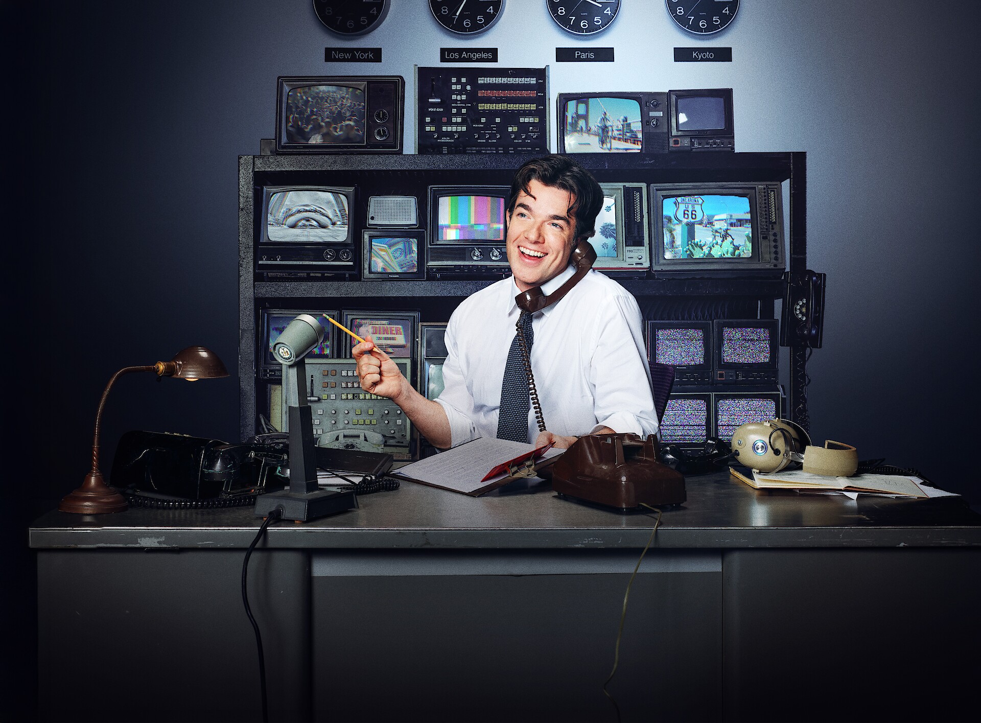 Everybody’s Live with John Mulaney key art - John Mulaney sitting at a desk in front of a bank of tvs