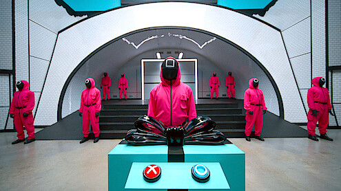 Guards in pink uniforms and masks stand in a futuristic, sterile room; one stands behind a control panel with red and blue buttons, creating a tense, mysterious atmosphere.