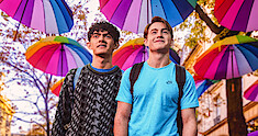 Joe Locke as Charlie and Kit Connor as Nick walk through the streets of Paris with umbrellas hanging above them in Season 2 of 'Heartstopper."