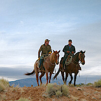 2 men on riding horses in the open terrain