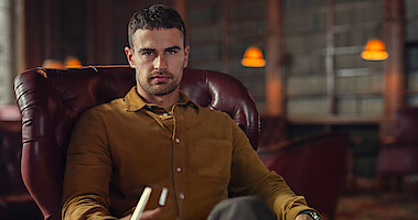 Theo James as Eddie Horniman in The Gentlemen sits in an office holding a glass of wine in Season 1 of 'The Gentleman'
