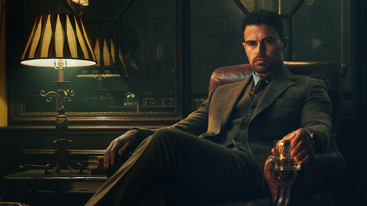 Theo James as Eddie Horniman in The Gentlemen sits in a leather chair holding a glass in Season 1 of 'The Gentleman'