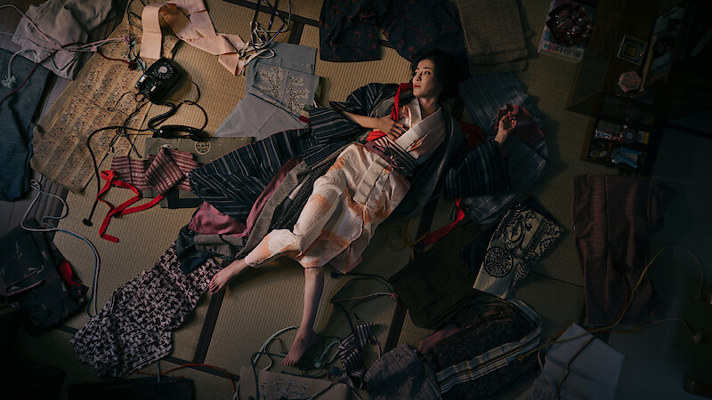 A still image from 'Asura' depicts a woman on the ground surrounded by clothes. 